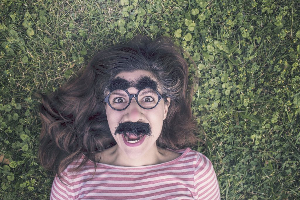 woman lying in grass wearing disguise glasses and mustache